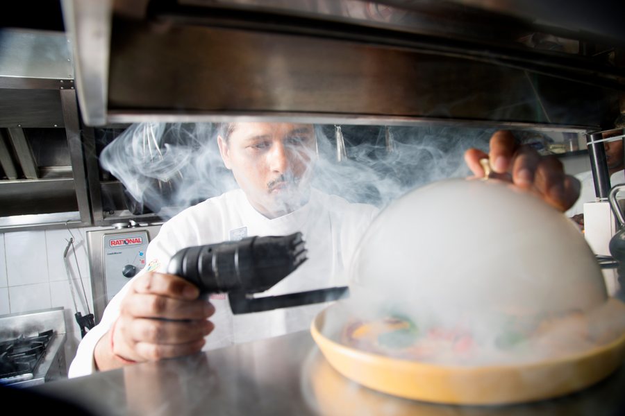 Chef finishing a dish beneath aromatic smoke